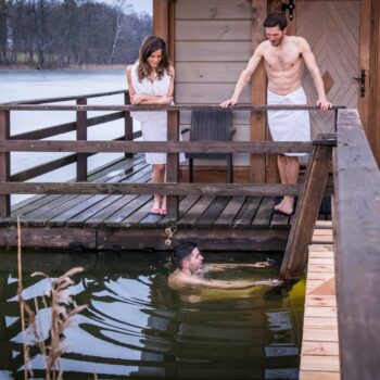 Dwie osoby stoją na pomoście przez Ruską Banią, trzecia osoba kąpie się w jeziorze